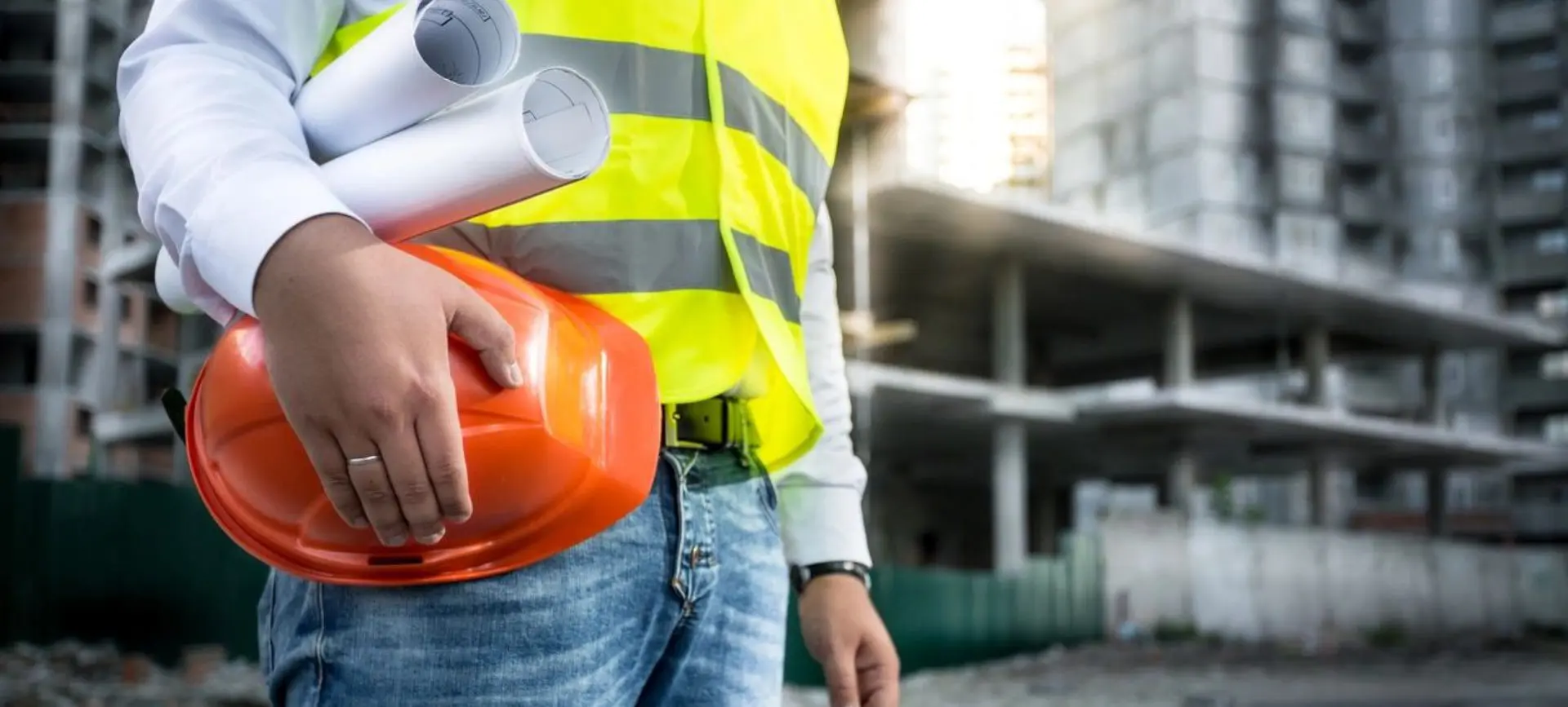 A construction worker holding an orange helmet and some papers.