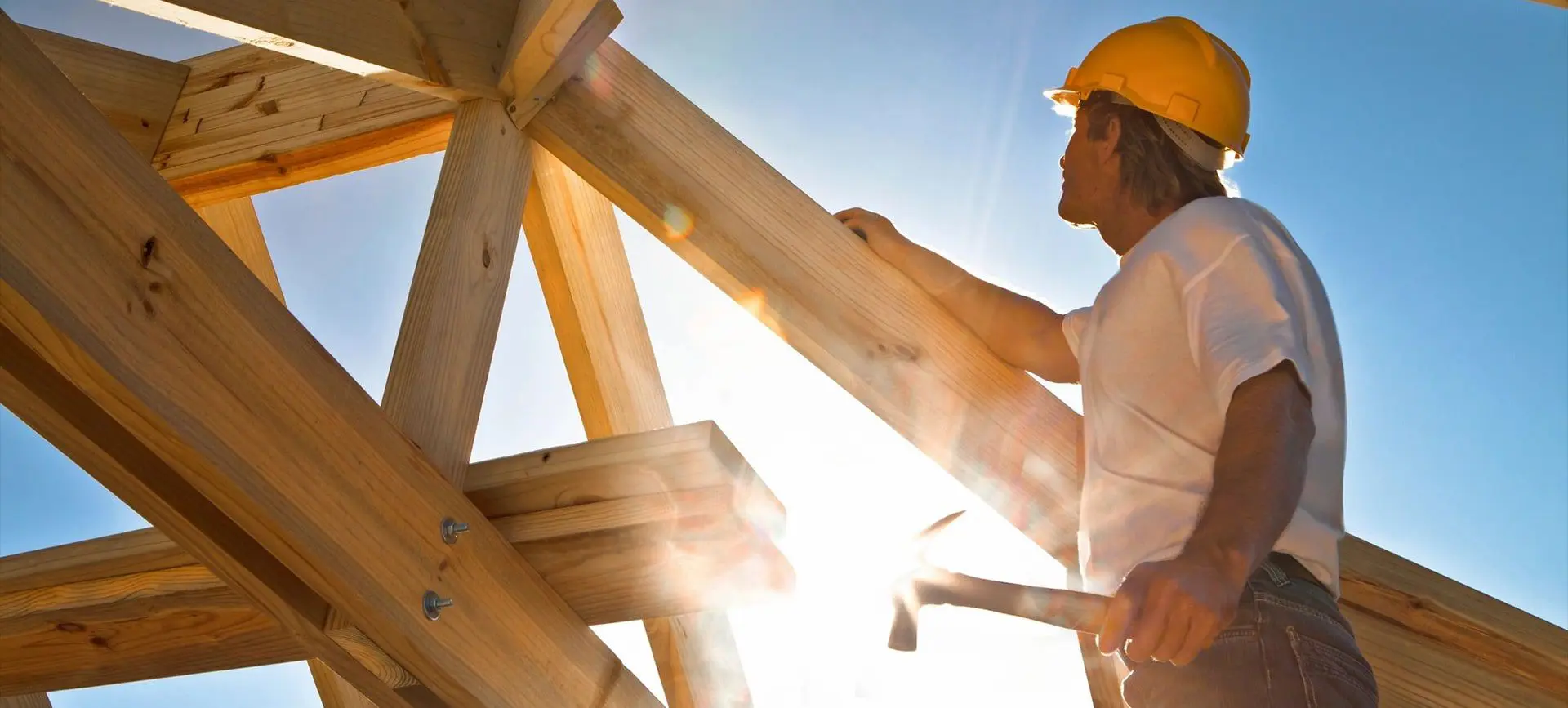 A man in yellow hard hat working on wooden structure.