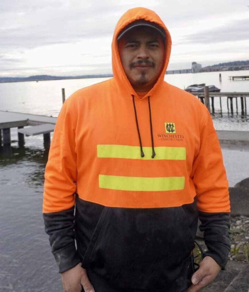 A man in an orange and black jacket standing on the beach.