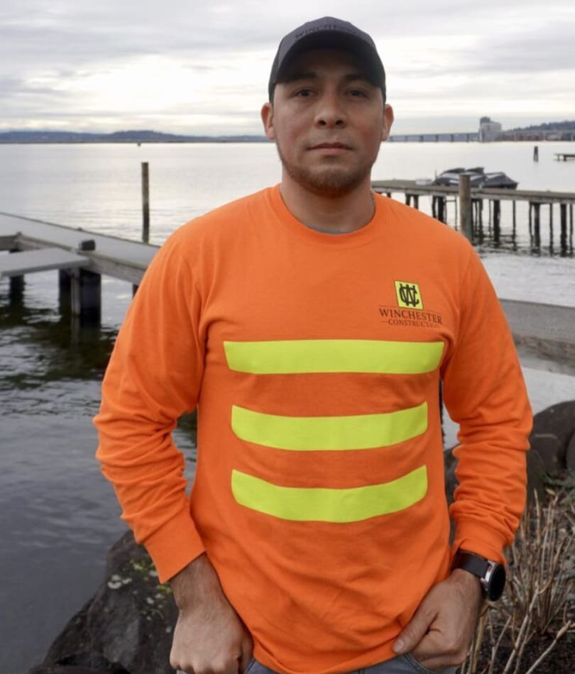 A man in an orange shirt standing next to water.