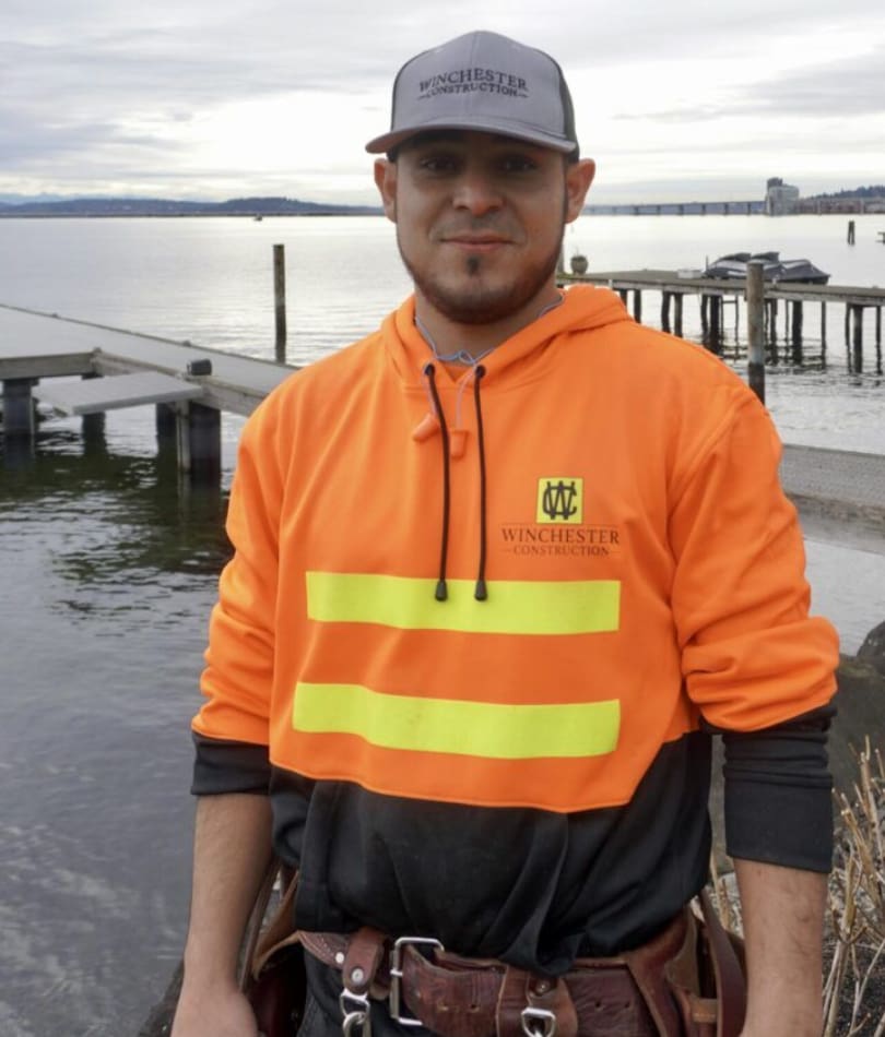 A man in an orange and black jacket standing next to water.